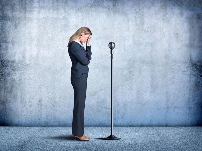 マイクの前に立って、顔を覆いうなだれる女性