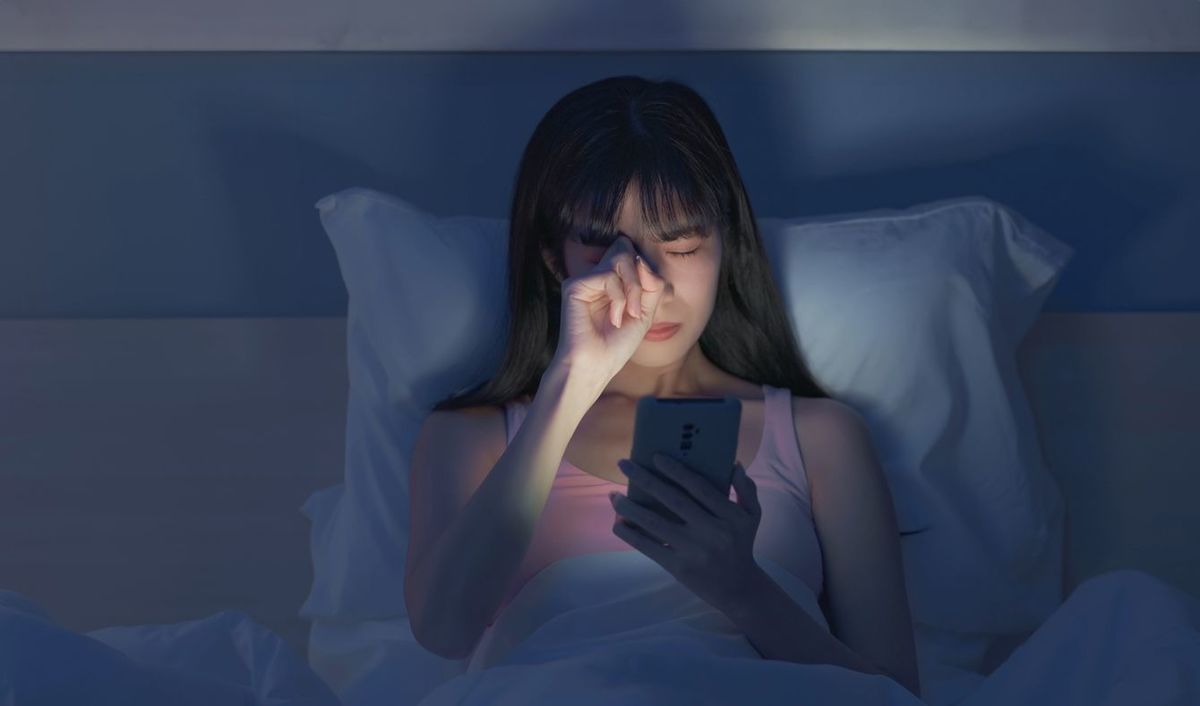 ベッドで夜にスマホを見て眩しい女性