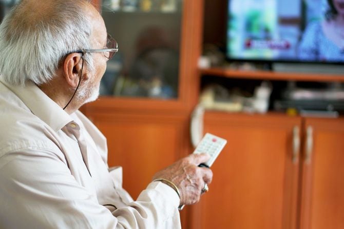 リモコンでチャンネルを変えながらテレビを見ているシニア