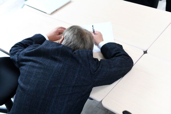 オフィスの机で過労で倒れるシニア実業家