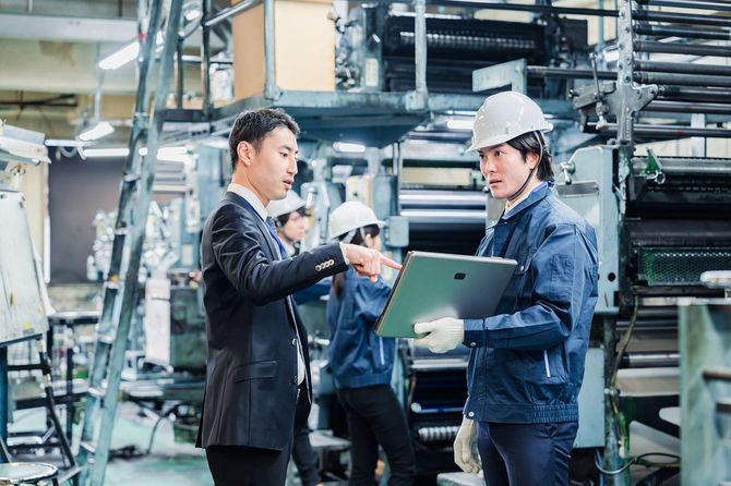 工場の作業員と話をするスーツの男性