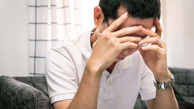 顔に手を当てストレスを感じている男性