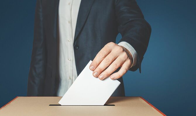 認識できない男性有権者は、投票箱の上に投票用紙を手に持っています