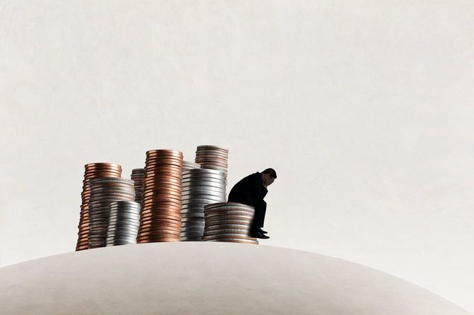 積み上げて置かれたコインに腰掛け、手で顔を覆って嘆いている人