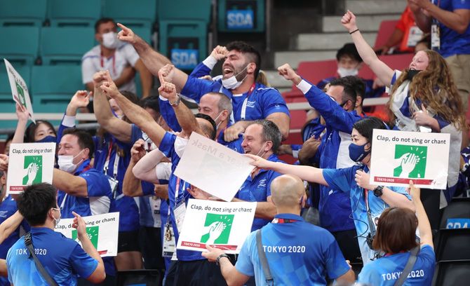柔道会場で応援のため盛り上がる関係者席。手前はマスク着用を促す掲示物を掲げるスタッフ＝2021年7月31日、東京・日本武道館