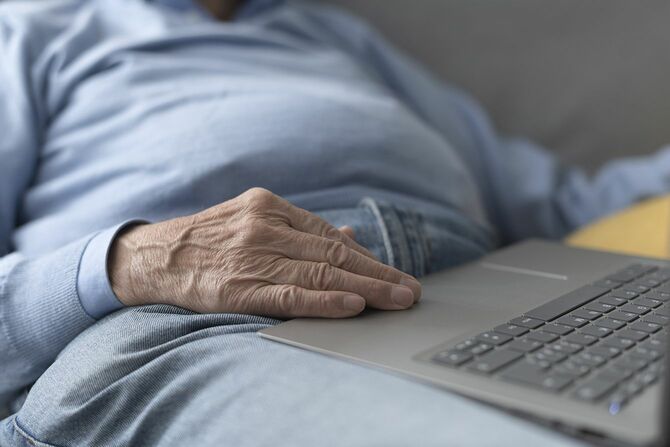 ソファに座ってパソコンを使用する高齢者
