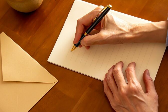 テーブルの上に置かれたひな形、封筒、ボールペン、コーヒー、ペンを持つ手