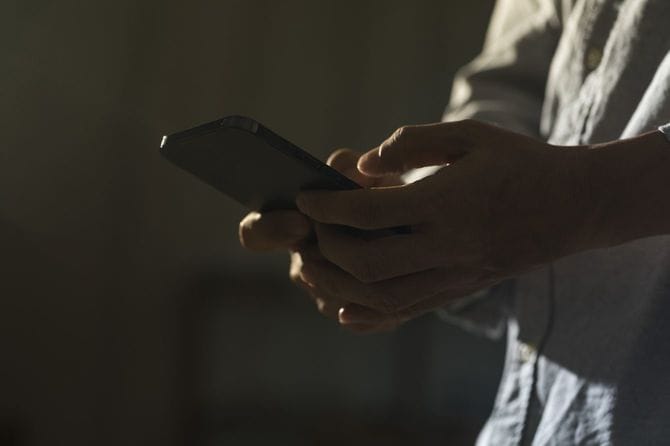 暗がりでスマートフォンを使用している男性の手元