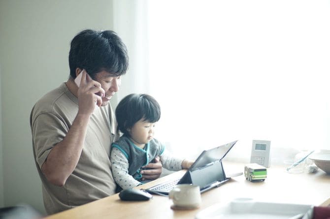 息子を膝に乗せて自宅で働く父親
