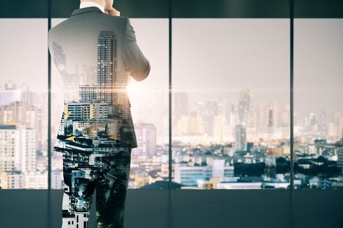 市街の景色を望むオフィスに立つ若いビジネスマン