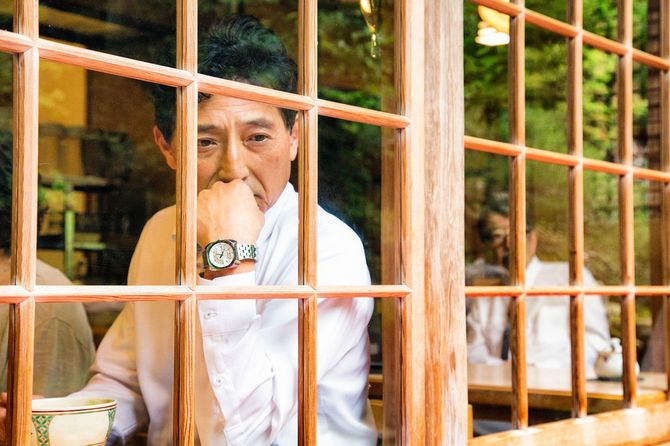 頬杖をついて窓際に座っている中年の男性