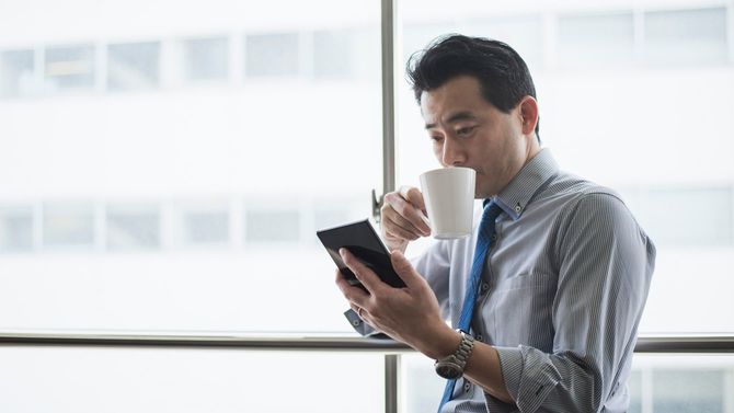 オフィスでコーヒーを飲みながらタブレットを使用する男性