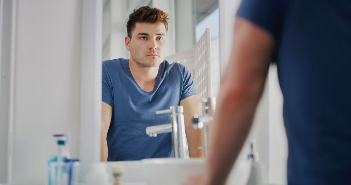 洗面台の鏡に映る自分を見つめる男性