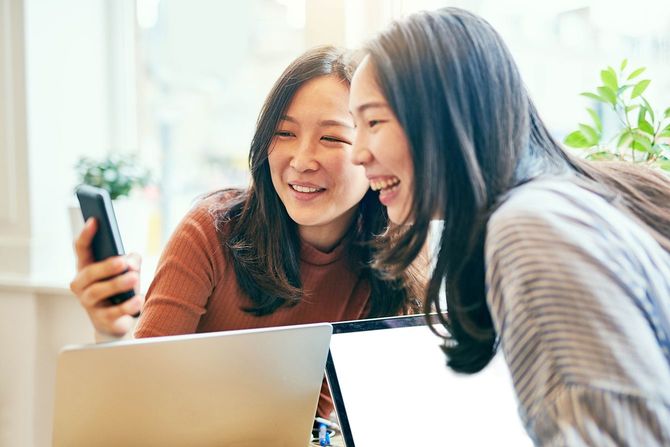 一緒に喫茶店で冷やしながら携帯電話を見ている2人の若いガールフレンドのクロップドショット