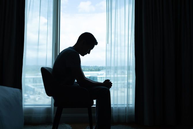 窓辺でうなだれている男性のシルエット