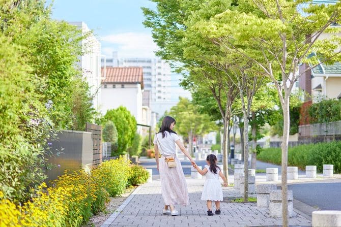 娘の手を引いて住宅街を歩く若い母親