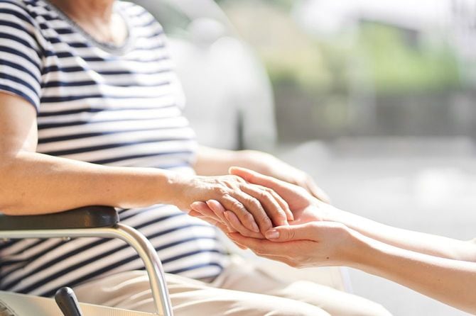 車椅子に乗っているシニア女性の手をとる介助者