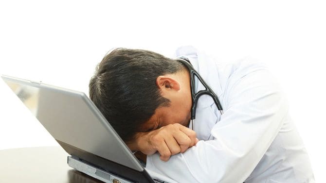 疲労した医師が机でうつぶせになっている