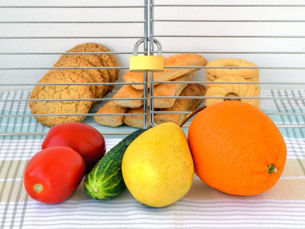 南京錠でロックされたケージの中にあるクッキーと扉の前面に置かれた野菜と果物