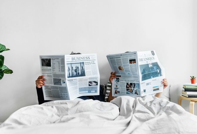 アジアのカップルがベッドで新聞を読む