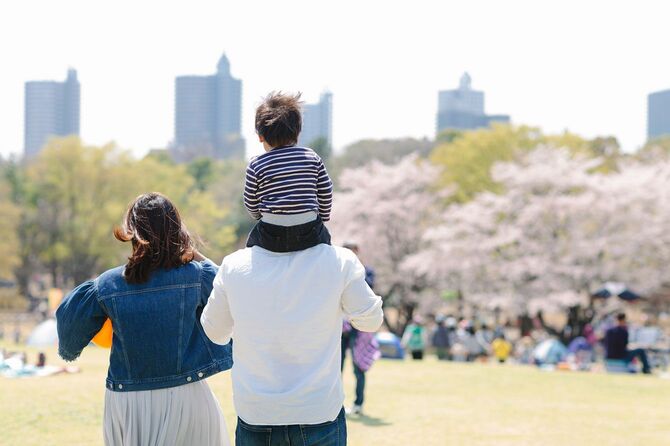 桜の咲く公園で子供を肩車して歩く親子連れ