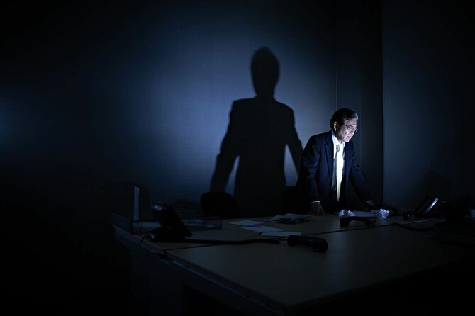 会社の暗い部屋でパソコン画面を見ながら立ち尽くす男性