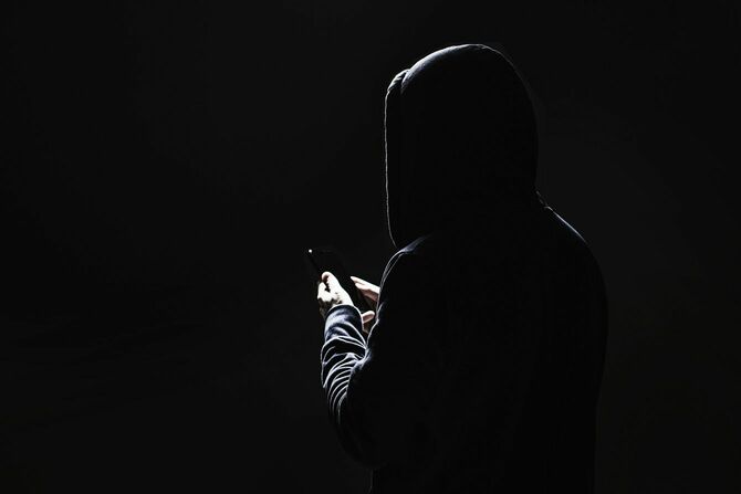 黒い背景にスマートフォンを操作する黒い服装の男性