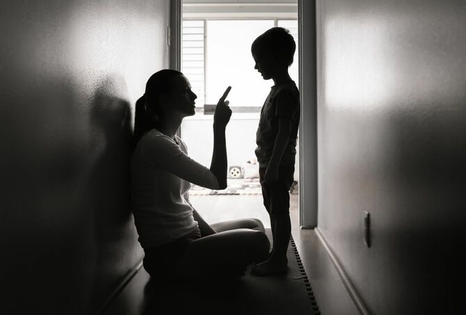 狭い廊下に座り込み、指をさして子を叱る母親