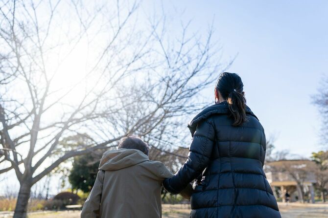 高齢の女性の腕を支え公園を歩く女性