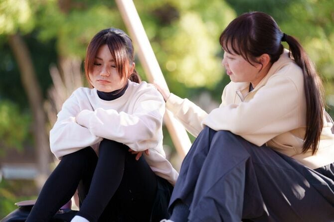公園で二人の女性の友人が一緒に座り、会話の中で一人がもう一人を支え合う