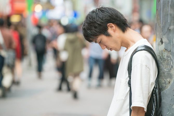 電柱にもたれかかってうつむく若い男性