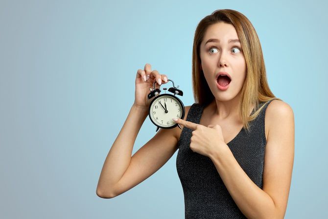 目覚まし時計を手に、驚いた表情をしている女性