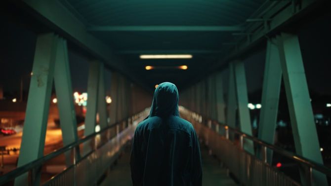 パーカーのフードをかぶり、歩道橋をわたっている男性の後ろ姿