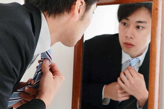 鏡を見てネクタイを締める男性
