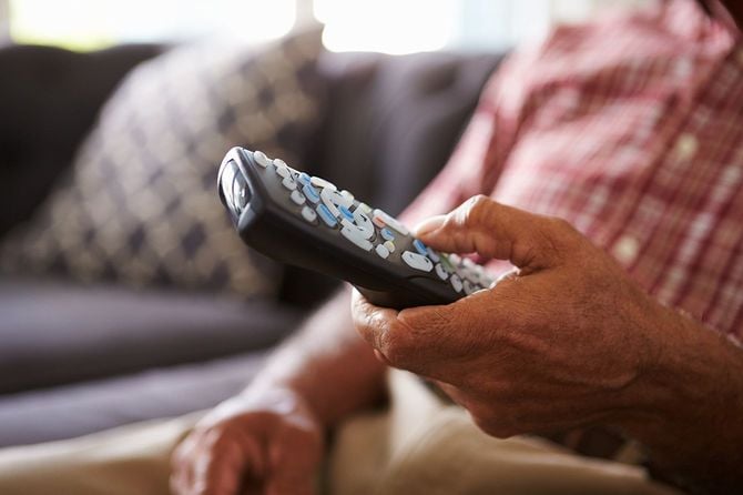 ソファに座っているシニアマンのクローズアップテレビリモコン