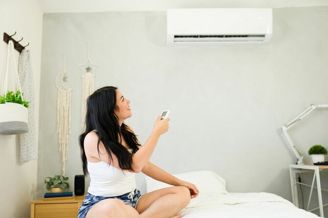 ベッドに座りエアコンを操作する女性