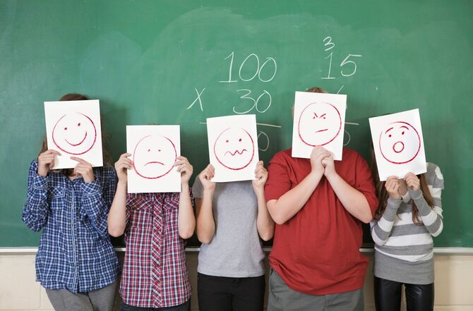 黒板の前でさまざまな表情を描いた画用紙を顔の位置に持っている生徒たち