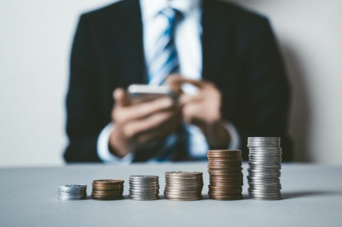 硬貨ごとに積み上げたコインを前に、スマホを使用している男性