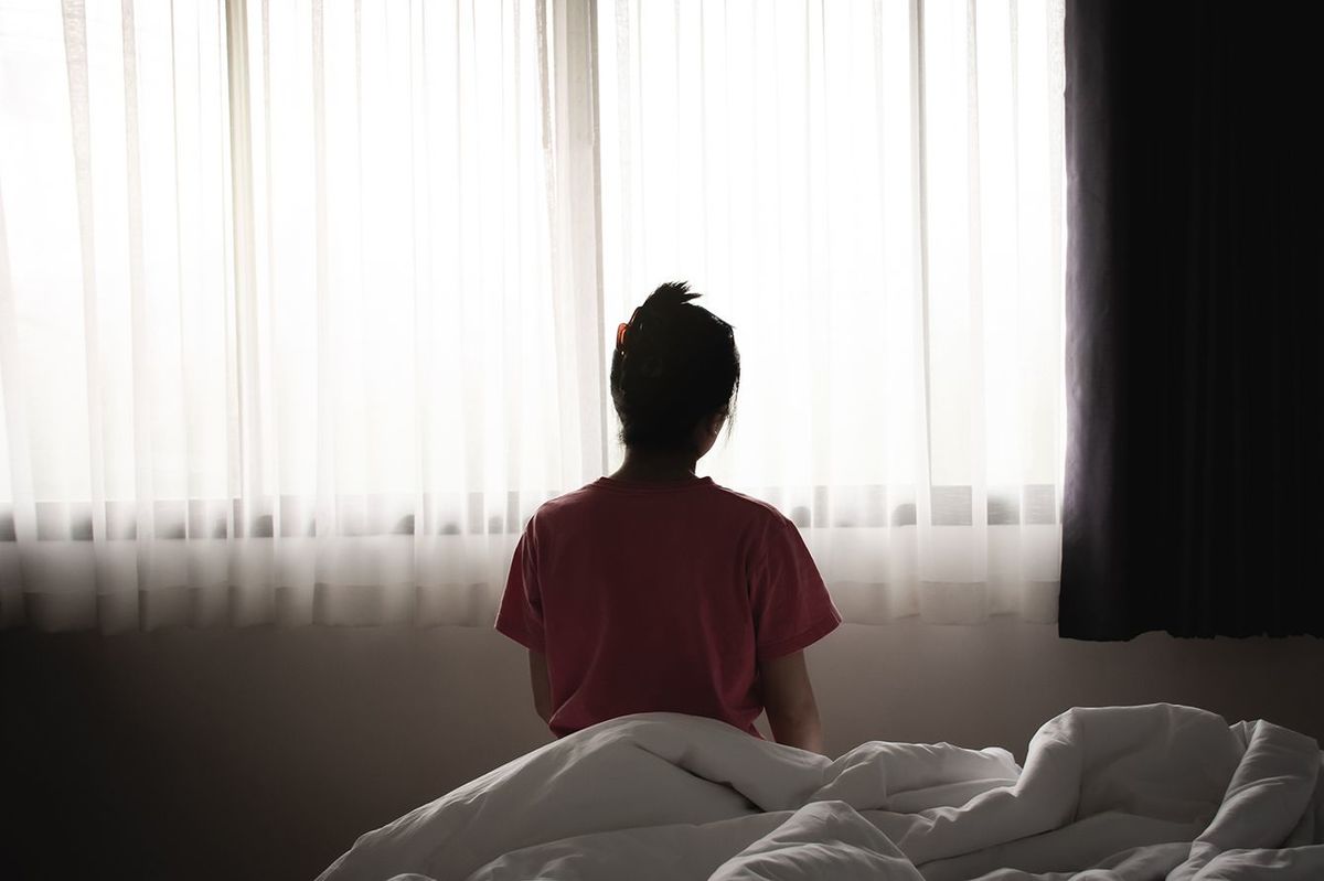 うつ病のアジアの女性は、朝ベッドに座って悲しいと孤独な感じを持っています。
