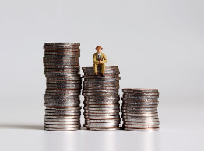 硬貨の山の上に座っているミニチュア男