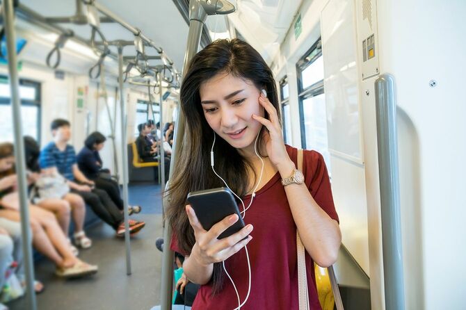 地下鉄で携帯電話を介して歌を聞くアジア女性