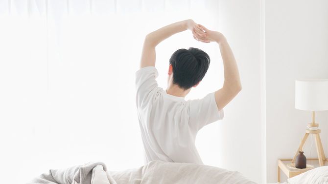 陽の光が照らすベッドの上でストレッチする男性