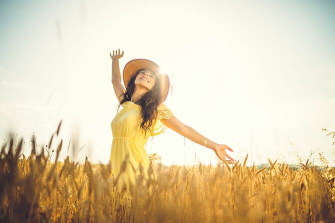 晴れた日に小麦畑で両手を広げている幸せそうな若い女性