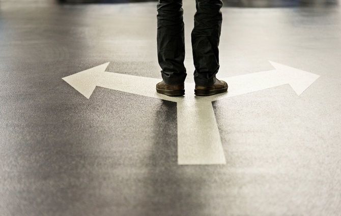 分かれ道の矢印の上に立つ人