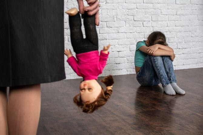 子どもの人形を取り上げる親と、膝を抱えて顔をうずめる子ども