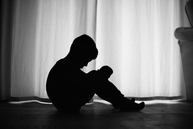 家の床に座っている悲しい少年