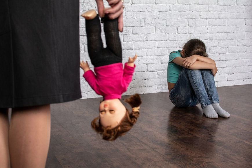 子どもの人形を取り上げる親と、膝を抱えて顔をうずめる子ども