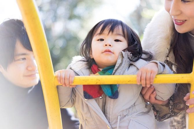 公園の遊具で遊ぶ子供の両隣で支え、見守る両親
