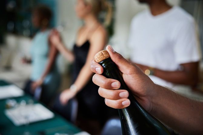 友人とのディナーパーティーでシャンパンのボトルを開ける若者