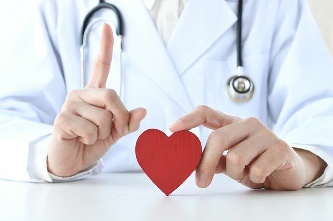人差し指と赤いハートの物体を立てる医師